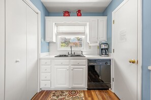 A compact kitchen with white cabinetry, a built-in dishwasher, and a coffee maker. - Colington Harbour 34: Soundfront with Private Dock (Colington)