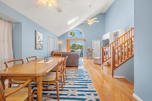 A spacious living area with a dining table, chairs, a sofa, and a staircase. - Colington Harbour 34: Soundfront with Private Dock (Colington)