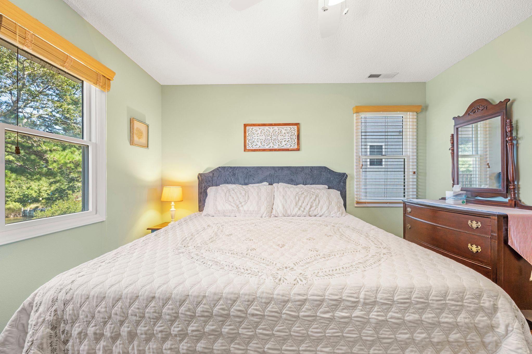 A bedroom with a large bed, a nightstand, a dresser, a mirror, and a window with blinds.