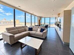 A modern living room with a sectional sofa, a dining area, and a kitchen. - Rokna corner penthouse - 240sqm with sea view in Xaghra Gozo (Ix-Xagħra)