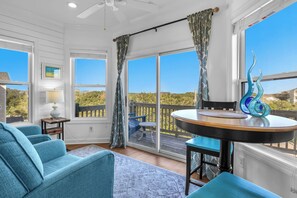 A room with a round table, blue chairs, a ceiling fan, and a view of a wooden deck and trees. - Shining Sea at North Topsail Beach, Steps to the Beach, Dog Friendly (North Topsail Beach)