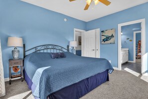 A bedroom with a bed, nightstands, a ceiling fan, and a door leading to another room. - Shining Sea at North Topsail Beach, Steps to the Beach, Dog Friendly (North Topsail Beach)