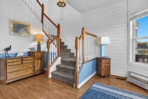 A staircase with wooden railings leading to a landing, a blue wall, and a window with a view. - Shining Sea at North Topsail Beach, Steps to the Beach, Dog Friendly (North Topsail Beach)