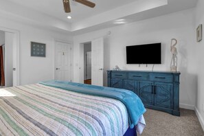 Quarto com cama, penteadeira, televisão e porta que dá para outro cômodo.