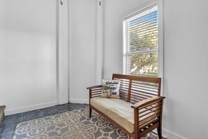 Quarto de canto com um banco, um tapete estampado e uma janela com persianas.
