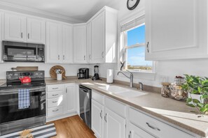 A modern kitchen with white cabinetry, stainless steel appliances, and a window providing a view. - Shining Sea at North Topsail Beach, Steps to the Beach, Dog Friendly (North Topsail Beach)