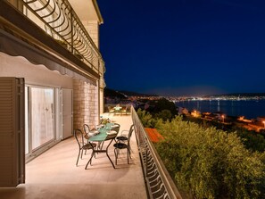 A balcony with a table and chairs, overlooking a coastal cityscape at night. - Villa in Seget Donji With Swimming Pool (Seget)