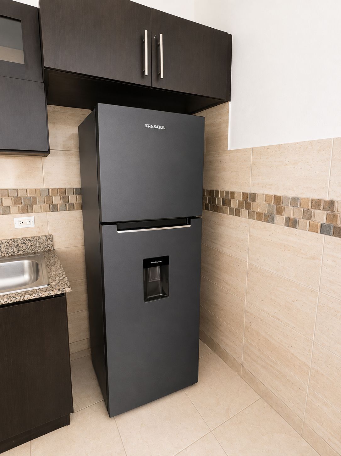 Un réfrigérateur noir doté d’un distributeur d’eau, situé dans une cuisine dont les murs sont recouverts de carreaux et le plan de travail est en granit.