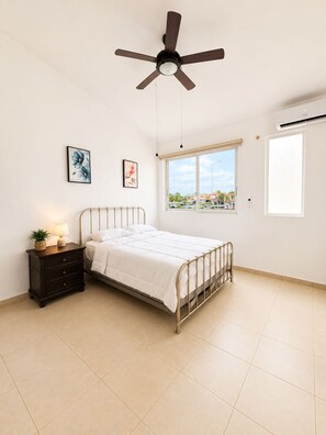 A bedroom with a bed, bedside table, lamp, and a ceiling fan.