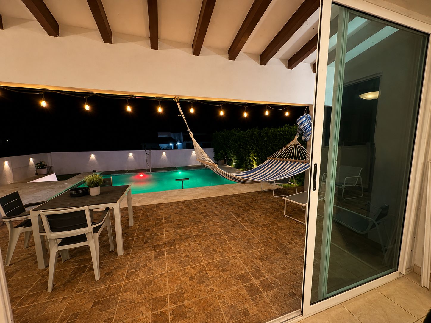 Un patio al aire libre con piscina, una hamaca y un comedor con sillas y una mesa.
