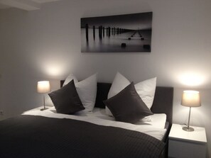 A bedroom with a bed, two bedside lamps, and a wall-mounted picture. - Holiday Apartment With 1 Bedroom (Bünsdorf)