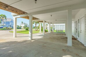 A covered outdoor area with concrete flooring, white pillars, and a view of a residential street with houses and palm trees. - NEW | Waterfront Getaway | Pet-friendly | Just a 2-minute walk to the beach (Galveston)