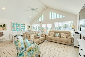 A spacious living room with a high ceiling, a ceiling fan, and a large window providing natural light. - NEW | Waterfront Getaway | Pet-friendly | Just a 2-minute walk to the beach (Galveston)
