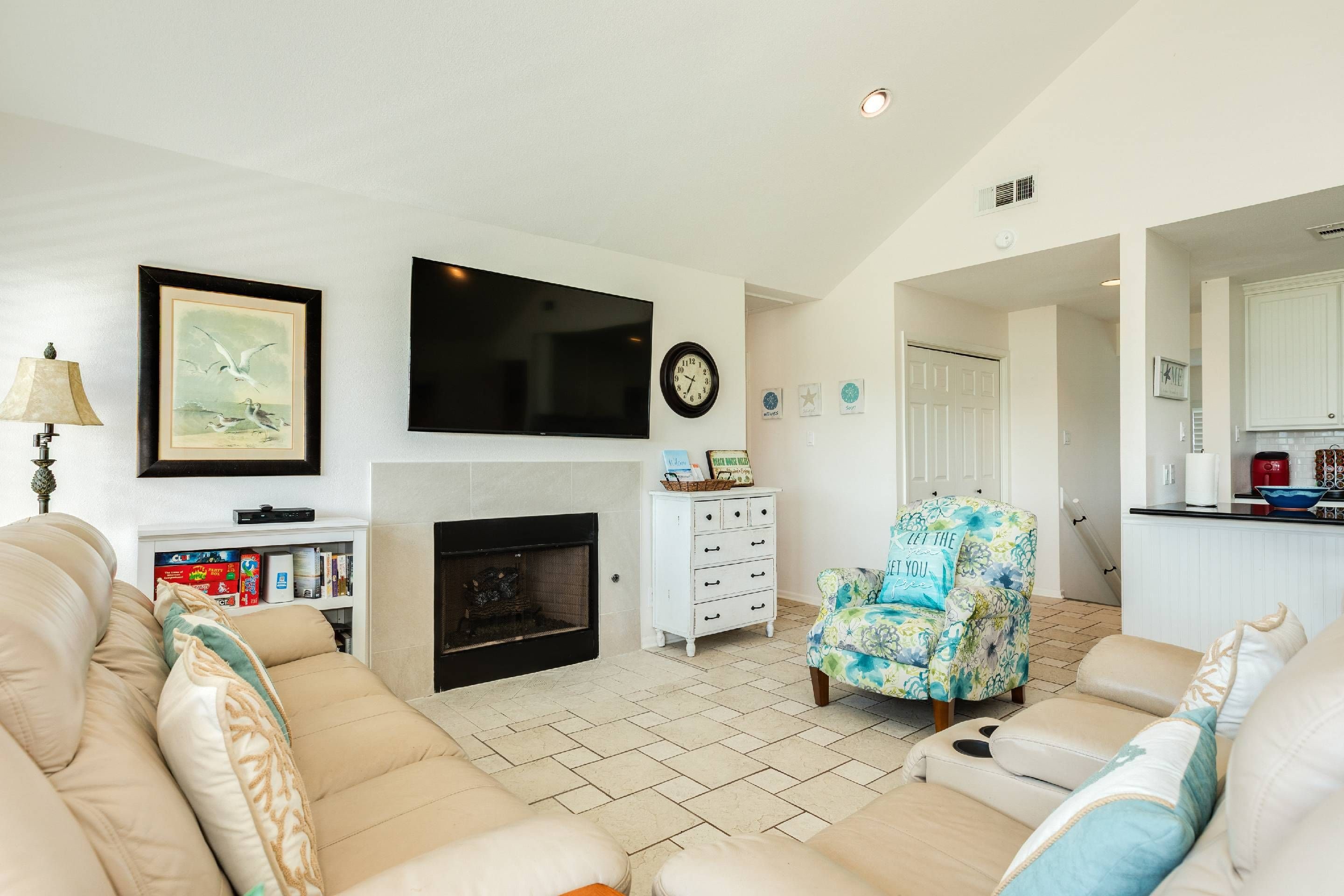 Una sala de estar con chimenea, televisor y un comedor con una cocina al fondo.