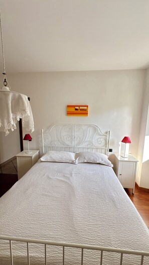 A neatly made bed with a white headboard and a textured white bedspread. There are two bedside tables with lamps, one on each side of the bed. - Sopramonte Apartment and Annex (Sopramonte)
