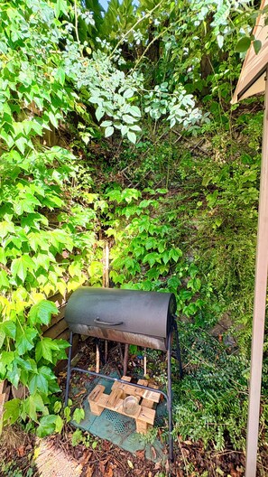 A metal barbecue grill with a wooden support structure, surrounded by dense green foliage. - Sopramonte Apartment and Annex (Sopramonte)