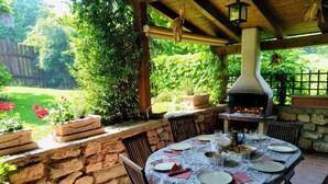 Eine Terrasse im Freien mit einer Steinsäule, einem runden Esstisch und einem Holzofen für Pizza.