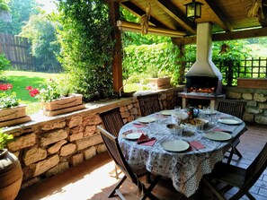 Un patio al aire libre con un muro de piedra, una mesa redonda preparada para comer y un horno de leña para pizzas.