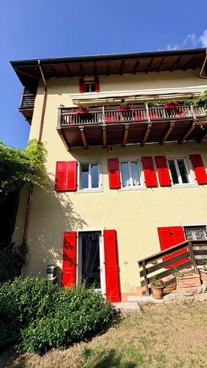 A two-story building with red shutters, a balcony, and a small garden area. - Sopramonte Apartment and Annex (Sopramonte)