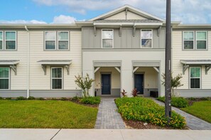 A two-story residential building with a symmetrical facade, a central entrance with a dark-colored door, and a small front garden with flowers and shrubs. - 5BR townhouse sleeps 14 with game room (Clermont)