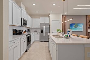 Une cuisine moderne avec des meubles blancs, des appareils en acier inoxydable et un grand îlot central doté d’un évier.