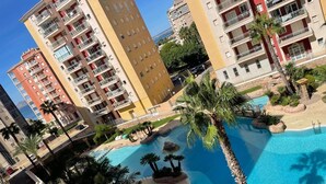 Et boligkompleks med flere altaner og en swimmingpool omgivet af palmer.