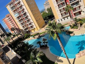 Conjunto de edifícios residenciais com várias varandas e uma piscina rodeada por palmeiras.