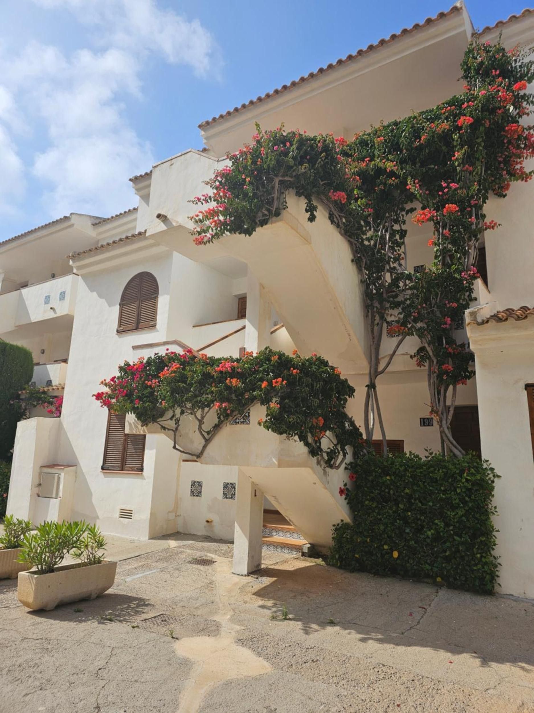 Un edificio con fachada blanca, una escalera y enredaderas con flores.
