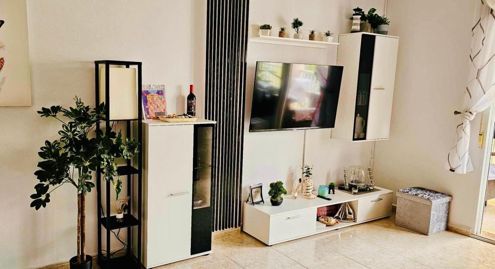 Ein Wohnzimmer mit Flachbildfernseher, einem weißen Schrank, einer Pflanze und einem kleinen Tisch mit Dekoration.