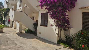 Ein Wohngebäude mit einer Treppe zu einem Balkon, umgeben von einem Garten mit Bougainvillea.