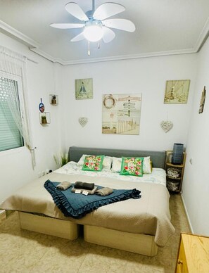 Quarto com cama, ventoinha no teto, decorações nas paredes e janela com persianas.