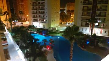 A nighttime view of a hotel with a swimming pool surrounded by palm trees and illuminated by street lights.