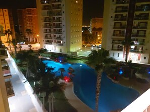 A nighttime view of a hotel with a swimming pool surrounded by palm trees and illuminated by street lights.