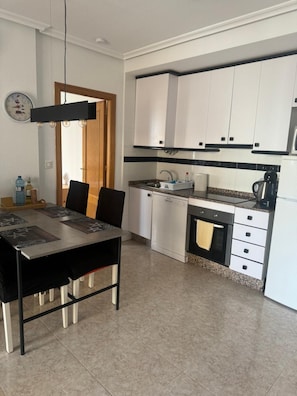Una cocina moderna con armarios blancos, encimera negra y un comedor con mesa y sillas.