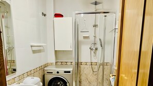Et badeværelse med toilet, vask, brusebad og vaskemaskine.