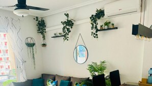 En moderne stue med sofa, sofabord og spisebord. Planter står på hylder og der hænger en plante.