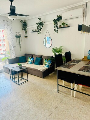 Uma sala de estar moderna com um sofá, mesa de centro e mesa de jantar. Há plantas em prateleiras e uma planta suspensa.