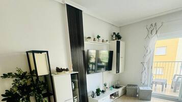 En moderne stue med fjernsyn, reoler og en potteplante.