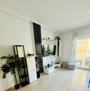 A modern living room with a TV, shelving, and a potted plant.