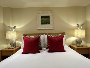 Quarto de hotel com cama, duas mesinhas de cabeceira, duas luminárias e um quadro na parede.