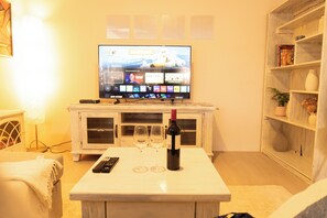 A living room with a television on a stand, a wine bottle, and two glasses on a table.