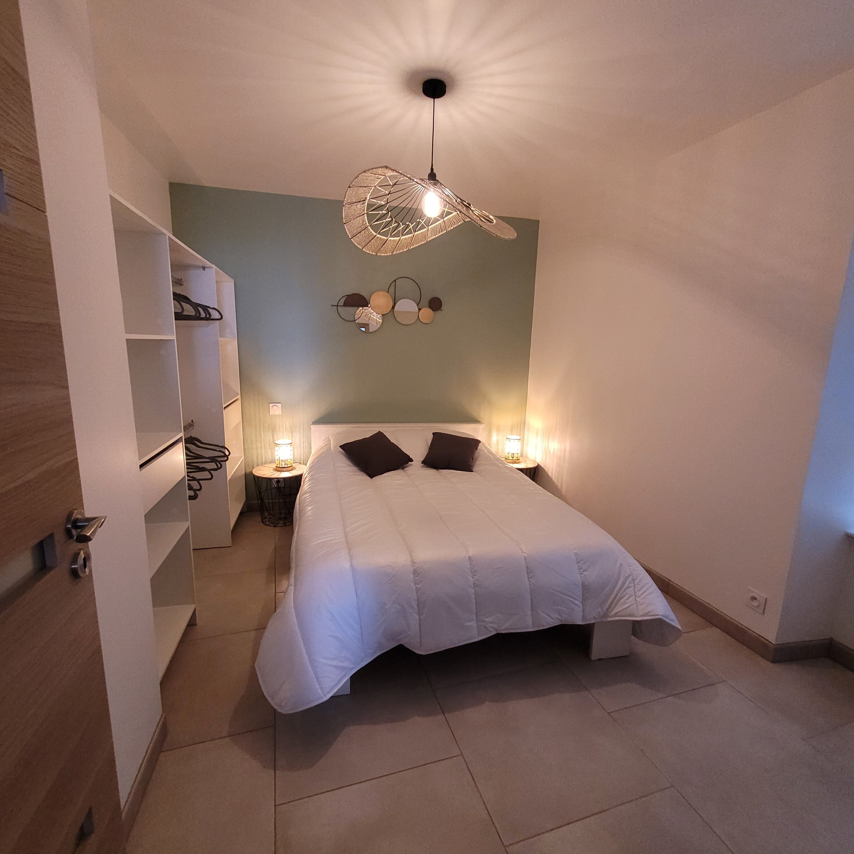 A bedroom with a bed, bedside lamps, a wall-mounted light fixture, and a shelving unit.