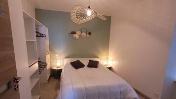 A bedroom with a bed, bedside lamps, a wall-mounted light fixture, and a shelving unit.