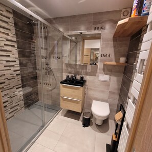 Een moderne badkamer met een douchecabine van glas, een houten wastafelmeubel en een toilet.
