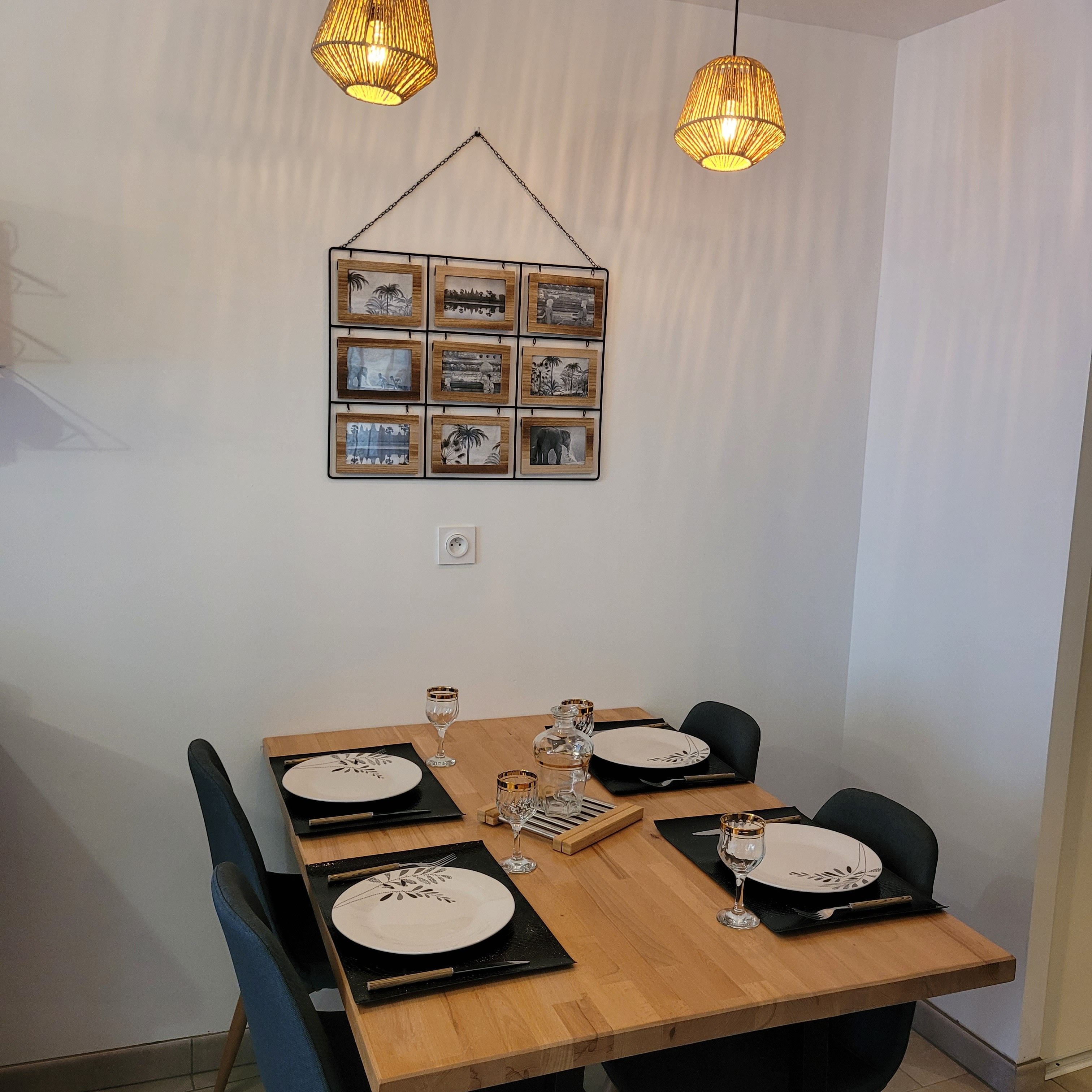 A dining area with a wooden table set for four, featuring black placemats with white plates, clear wine glasses, and a small decorative item.