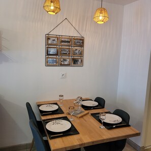 Een eetgedeelte met een houten tafel gedekt voor vier personen, voorzien van zwarte placemats, witte borden, glazen wijnglazen en een klein decoratief object.