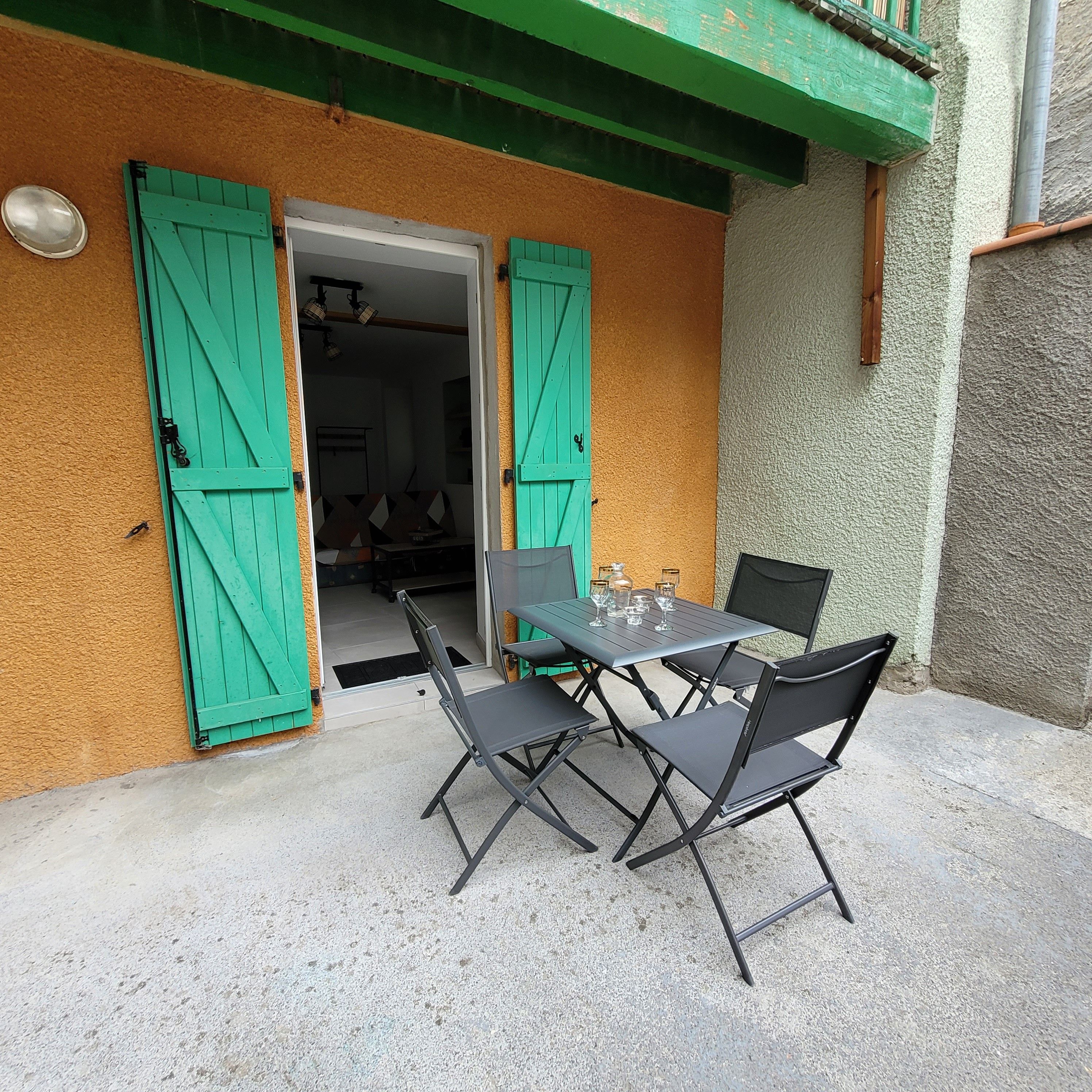 An outdoor seating area with a table and chairs, a green door, and a textured wall.