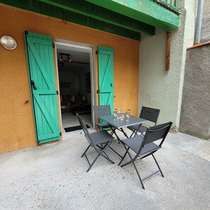 Een terras met een tafel en stoelen, een groene deur en een gestructureerde muur.