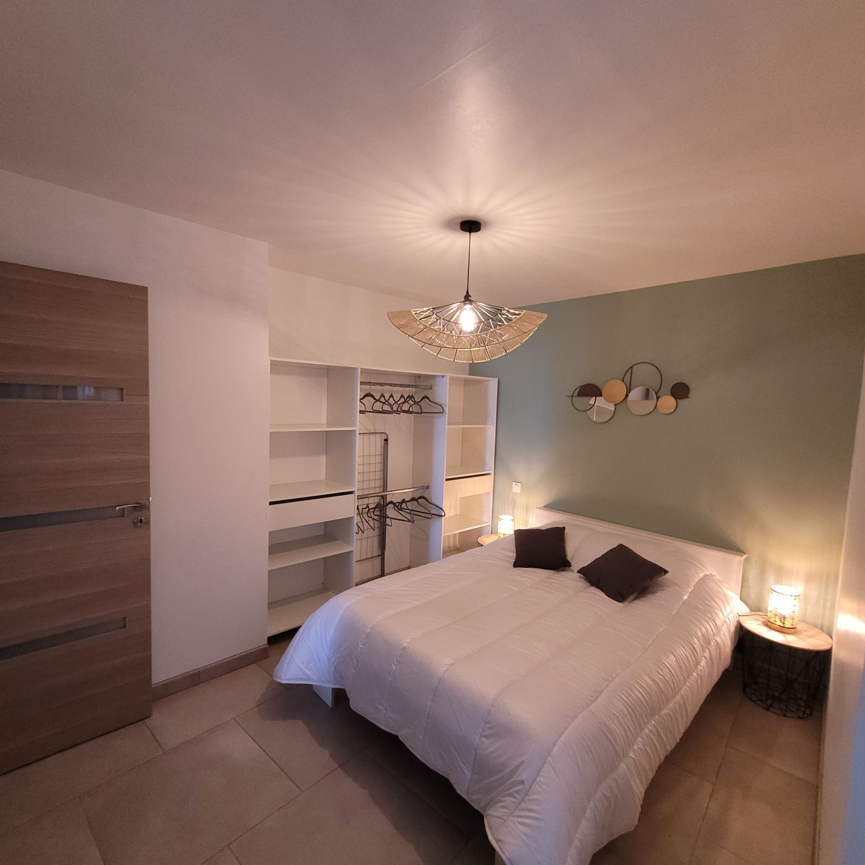 A bedroom with a large bed, a wardrobe, a walk-in closet, and a ceiling light fixture.