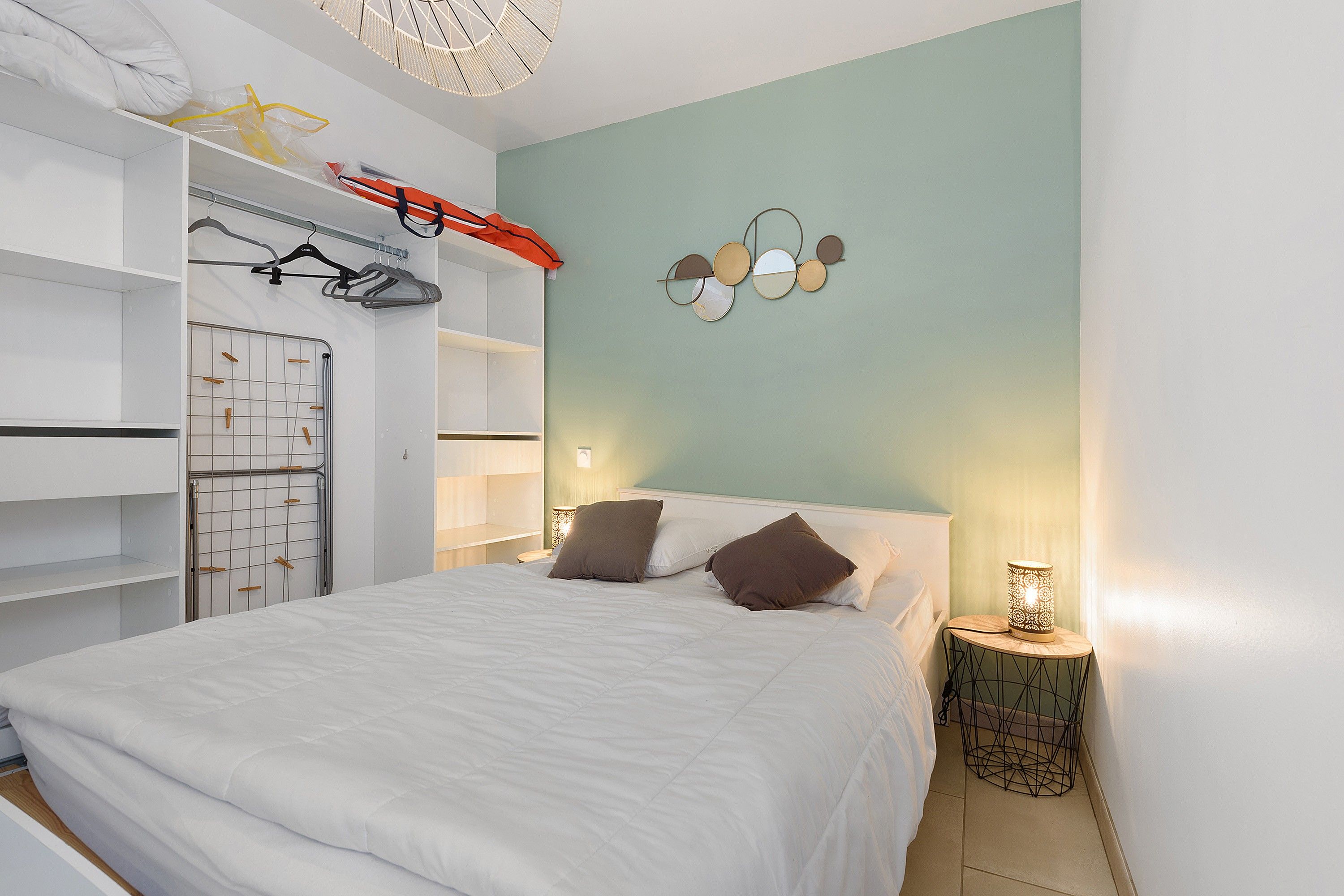 Une chambre à coucher comprenant un lit, une armoire, un étendoir et un miroir fixé au mur.